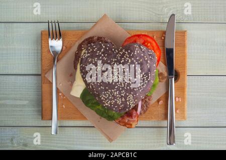 Herzförmige schwarz Hamburger, liebe Burger fast food Konzept, Valentinstag Überraschung zum Abendessen, Holz- Hintergrund, Ansicht von oben flach Stockfoto