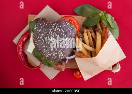 Herzförmige schwarz Hamburger, liebe Burger fast food Konzept, Valentines Tag überraschen Abendessen, roter Hintergrund, Ansicht von oben flach Stockfoto