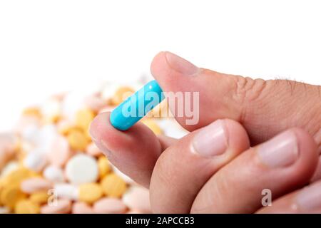 Hand hält eine blaue Pille über einem Haufen anderer verschiedener Pillen. Stockfoto