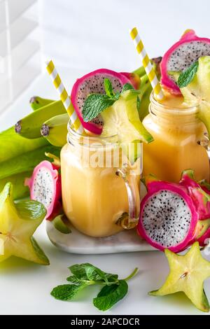 Eine Nahaufnahme von zwei exotischen Fruchtsmoothies in Glasgefäßen, umgeben von exotischen tropischen Früchten, bereit zum Trinken Stockfoto