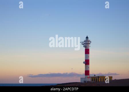 Küstenlandschaft von Teneras, in der der Leuchtturm von El Porís während des Sonnenuntergangs der Protagonist ist ist. Der blaue Himmel lässt Raum, um Texte oder Graphen hinzuzufügen Stockfoto