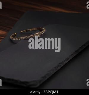 Goldenes Armband mit Diamanten auf schwarzen Steinplatten. Quadratischer Schuss aus goldenem Armband mit Rauten auf schwarzen Platten. Stockfoto