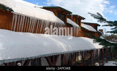 Eiszapfen und Schnee auf dem Dach des Holzgebäudes Stockfoto