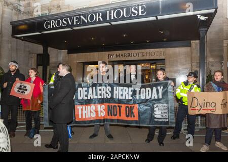 Park Lane, London, Großbritannien. Januar 2020. Demonstranten vor dem JW Marriott Grosvenor House Hotel mit Bannern mit der Aufschrift "WAFFENHÄNDLER HIER HEUTE - DAS IST NICHT OK" und anderen Schildern wie "STOPPT SAUDI BEWAFFNET" und "sterben für..." Zwei Polizisten sind anwesend; Kampagnenmarkierung für Kampagne gegen den Pelzhandel (CAFT) sichtbar. Die Szene dokumentiert eine öffentliche Demonstration, bei der Bedenken hinsichtlich der Tierrechte und des Pelzhandels geäußert werden. Aktivistengruppen Kampagne gegen den Waffenhandel mit Stop the Arms Fair Protest im Grosvenor House Hotel. Penelope Barritt/Alamy Live News Stockfoto