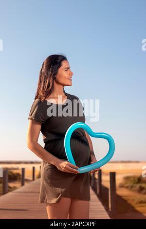 Schwangere Frau posiert mit blauem Herzballon auf den Marschländern. Stockfoto