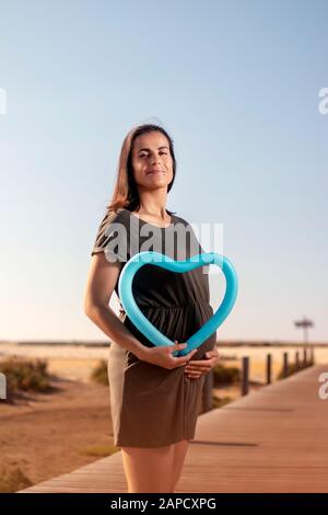 Schwangere Frau posiert mit blauem Herzballon auf den Marschländern. Stockfoto