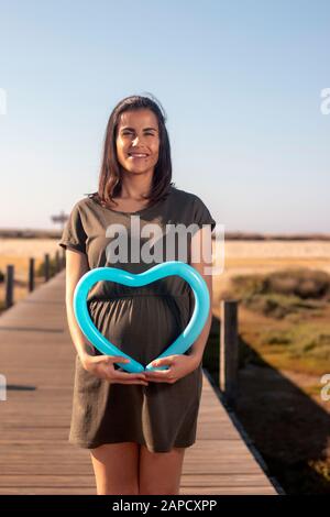 Schwangere Frau posiert mit blauem Herzballon auf den Marschländern. Stockfoto