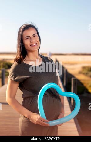 Schwangere Frau posiert mit blauem Herzballon auf den Marschländern. Stockfoto