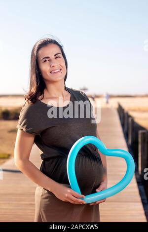 Schwangere Frau posiert mit blauem Herzballon auf den Marschländern. Stockfoto