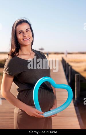 Schwangere Frau posiert mit blauem Herzballon auf den Marschländern. Stockfoto