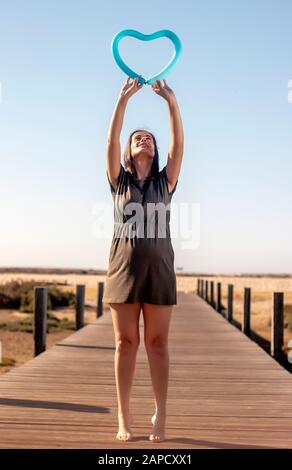 Schwangere Frau posiert mit blauem Herzballon auf den Marschländern. Stockfoto
