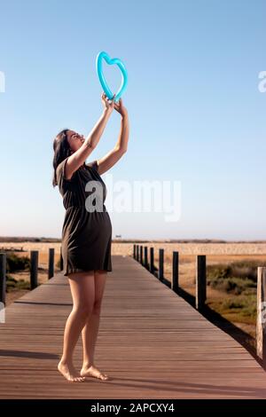 Schwangere Frau posiert mit blauem Herzballon auf den Marschländern. Stockfoto
