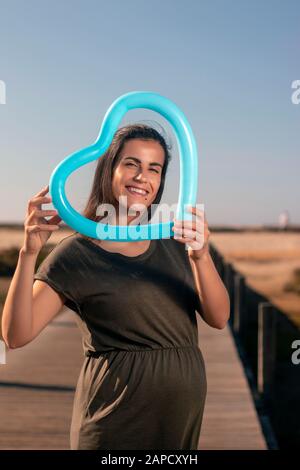 Schwangere Frau posiert mit blauem Herzballon auf den Marschländern. Stockfoto
