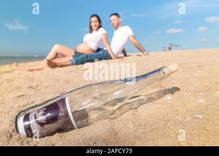 Schwangeres glückliches Paar posiert an der Strandlinie. Ultraschallfoto in der Flasche in Nahaufnahme. Stockfoto