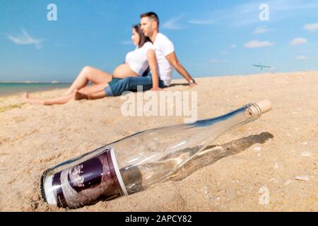 Schwangeres glückliches Paar posiert an der Strandlinie. Ultraschallfoto in der Flasche in Nahaufnahme. Stockfoto