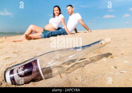 Schwangeres glückliches Paar posiert an der Strandlinie. Ultraschallfoto in der Flasche in Nahaufnahme. Stockfoto
