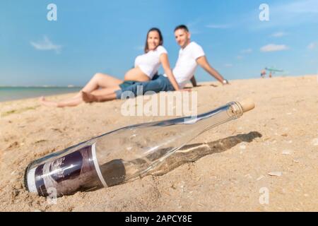 Schwangeres glückliches Paar posiert an der Strandlinie. Ultraschallfoto in der Flasche in Nahaufnahme. Stockfoto