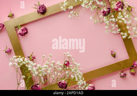 Kreativer goldener Rahmen mit getrockneten rosafarbenen Rosen auf pinkfarbenem Hintergrund. Grußkartenkonzept. Flaches Layout, Kopierbereich Stockfoto
