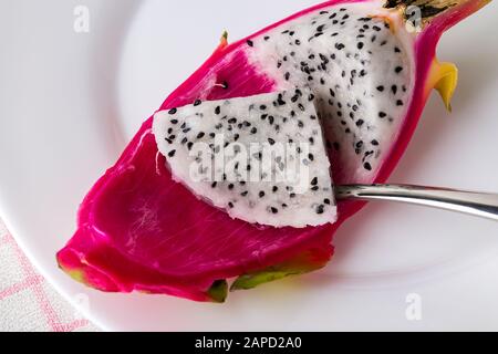 Nehmen Sie eine Drachenfrucht oder einen Pitaya-Fruchtfleisch mit einem Löffel auf einem weißen Teller. Obst und Gemüse. Gesunde vegetarische Kost mit B-Vitaminen und Tannin. Stockfoto