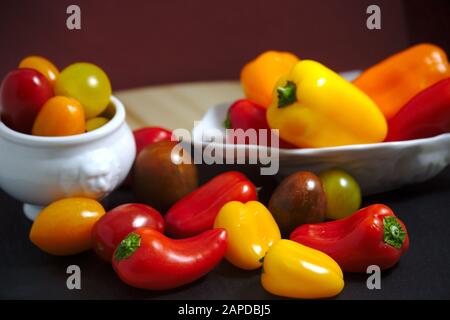 Ein Tisch mit einem Stillleben, bestehend aus kleinen Paprika, Kirschtomaten in roten und gelben Farben Stockfoto