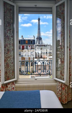 Ein Pariser Hotelzimmer mit Blick auf den Eiffelturm vom Hotel aus, Les Jardins d'Eiffel, Dächer und weiße Wolken des blauen Himmels. Stockfoto