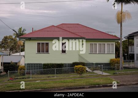 Grün lackiertes, niedrig angesetztes Vorstadthaus aus der Nachkriegszeit mit Flügelfenstern und rotem Wellblech in Cannon Hill, Brisbane, Australien Stockfoto