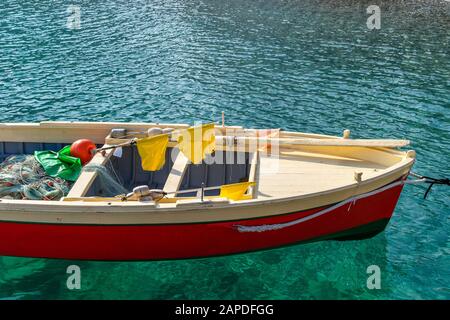 Teil eines kleinen Fischerboots, das an einem sonnigen Tag in leuchtend roten, beigen und grünen Farben im blauen Wasser der Mittelmeerküste gemalt wurde. Es gibt padd Stockfoto