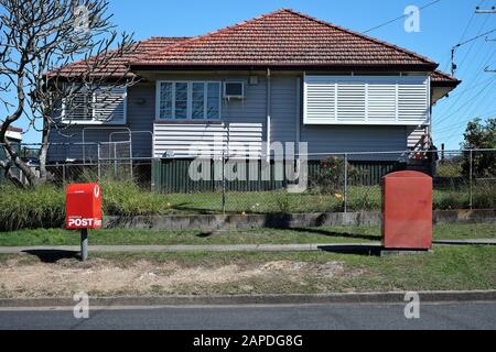 Zwei Rote Postboxen und ein originales Arbeiterhaus aus der Nachkriegszeit, rote Dachziegel, Flügelfenster, Wetterbrett auf niedrigen Baumstümpfen, in Carina, Brisbane Stockfoto