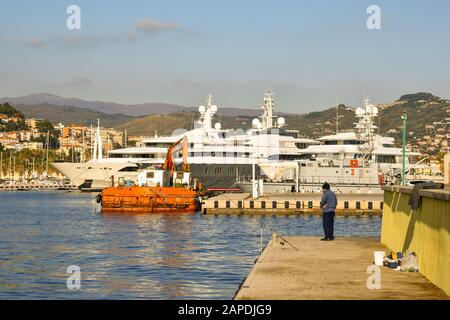 Blick auf den Touristenhafen von Porto Maurizio mit einem Fischer, der mit einem Stab am Kai angeln kann, und einer gefesterten Luxusyacht, Imperia, Ligurien, Italien Stockfoto