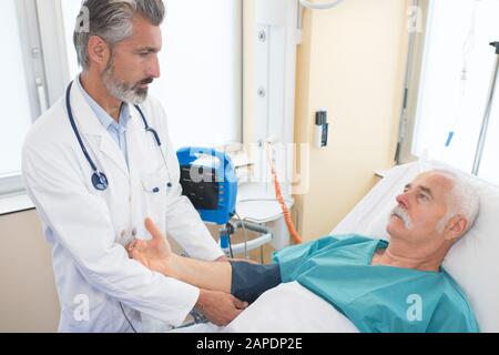 Der Arzt, der den Senior überprüft, bemannt den Blutdruck im Krankenhaus Stockfoto