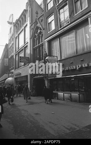 Kirchenbauten sind geschützt Beschreibung: Amsterdam, Kalverstraat. Eingang zum St. Petrus und Pauluskerk, genannt De Parrot zwischen den Schaufenstern mit Werbeschildern Datum: 28. Februar 1974 Ort: Amsterdam, Noord-Holland Schlüsselwörter: Architektur, Fassaden, Katholizität, Kirchenbauten, Neugotik, Portale, Stadtplastiken Stockfoto