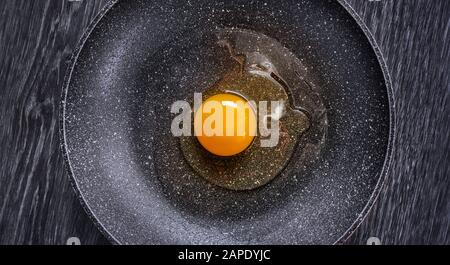 Ein rohes Ei in der Mitte einer Antihaftpfanne, symmetrisches Bild. Stockfoto