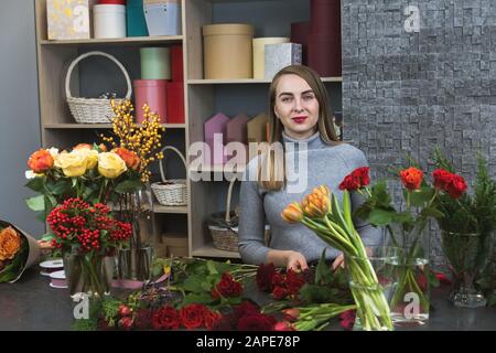 Kleine Unternehmen. Blumenhändler im Blumengeschäft unfokussiert. Studio mit Blumendesign. Süße geballte junge Floristin, die im Blumenladen arbeitet. Stockfoto