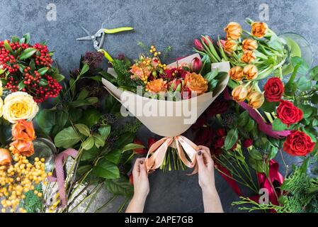 Das Konzept der Geschenke und Blumensträuße für den 8. März und Muttertag. Florist erstellt einen Blumenstrauß in einem Blumenladen. Ansicht von oben in einem wunderschönen Blumenstrauß aus roten, oder Stockfoto