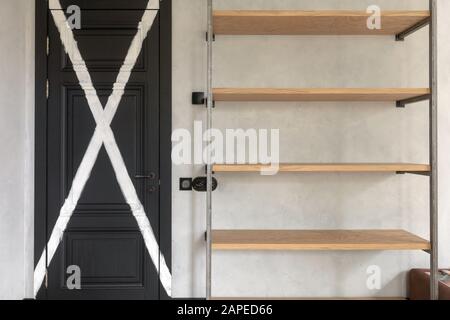 Schwarze Holztür mit weißem Kreuz neben leerem Gestell Stockfoto