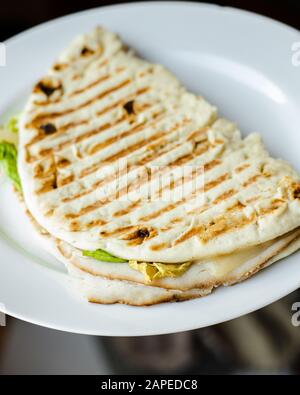 Gegrilltes Panini-Pita-Brot, türkei, schweizer Käse, Salat-Sandwich auf einer weißen Platte in der Nähe Stockfoto