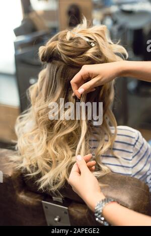 Der Friseur kreiert Locken und wellenförmige Haare in der Blondine. Die Hände des Friseursalons locken beim Kunden. Stockfoto