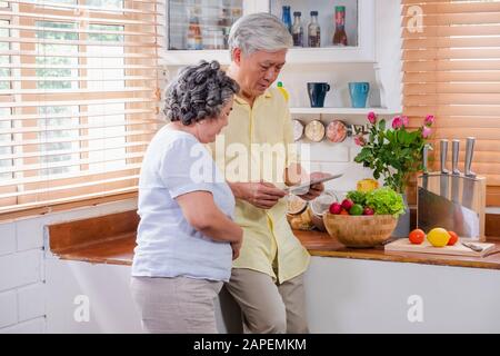 Asiatische senior Paar mit Tablet-PC zu suchen Menü Rezept und Art von Gemüse in der Küche zu Hause. Senior mit Technologie lfiestyle. Altern mit Stockfoto