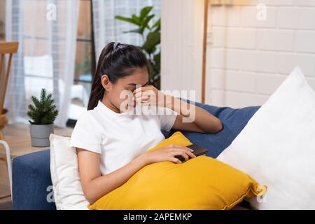 Junge asianerin, die Stress und geschlossene Augen spürt, leidet unter Kopfbedeckung auf dem Sofa im Wohnzimmer, müde Büroangestellte massa Stockfoto