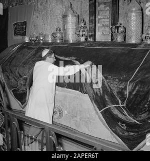 Israel 1964-1965: Jerusalem (Jerusalem), Kirchen und Klöster Beschreibung: Am Grabstein hebt der mutmaßliche Vormund/Gastgeber die Samtoberfläche, um eine ornamentierte Anmerkung zu zeigen: Das Grab befindet sich im Erdgeschoss und dient heute als Synagoge und Betraum. Der Grabstein ist mit einem Samttuch bedeckt und darauf Tora-Kronen aus Synagogenkreisen jüdischer Gemeinden, der Grabstein selbst hat Aufschriften und Verzierungen aus der Kreuzfahrerzeit. Die Letzte Abendmahlshalle und das Grab Davids befinden sich im selben Gebäude Datum: 1964 Ort: Israel, Jerusalem, Berg Zion Schlüsselwörter: Gräber, Stockfoto