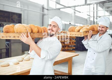 Zwei Bäcker Männer tragen die Fächer mit Brot in der Bäckerei. Stockfoto