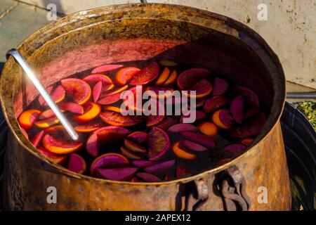 Glühwein wird in einem alten Kupfertopf zubereitet. Gelbe Zitronenscheiben schweben in rotem Glühwein. Stockfoto