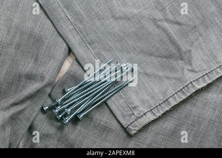 Eine Handvoll metallischer Selbstschneiderschrauben liegt vor dem Hintergrund eines alten Denimstoffs. Selektives Fokusmakro mit flachem Freiheitsgrad. Stockfoto