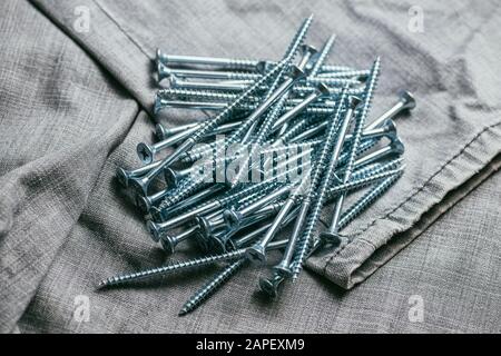 Eine Handvoll metallischer Selbstschneiderschrauben liegt vor dem Hintergrund eines alten Denimstoffs. Selektives Fokusmakro mit flachem Freiheitsgrad. Stockfoto