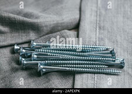 Eine Handvoll metallischer Selbstschneiderschrauben liegt vor dem Hintergrund eines alten Denimstoffs. Selektives Fokusmakro mit flachem Freiheitsgrad. Stockfoto
