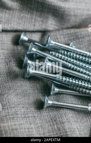 Eine Handvoll metallischer Selbstschneiderschrauben liegt vor dem Hintergrund eines alten Denimstoffs. Selektives Fokusmakro mit flachem Freiheitsgrad. Stockfoto