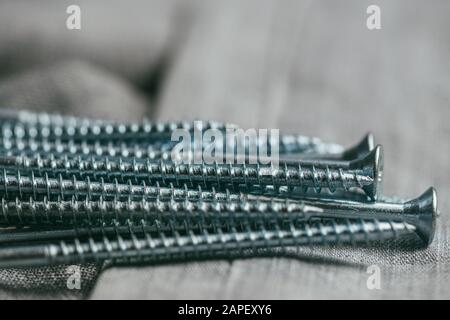 Eine Handvoll metallischer Selbstschneiderschrauben liegt vor dem Hintergrund eines alten Denimstoffs. Selektives Fokusmakro mit flachem Freiheitsgrad. Stockfoto