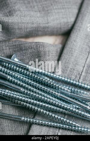 Eine Handvoll metallischer Selbstschneiderschrauben liegt vor dem Hintergrund eines alten Denimstoffs. Selektives Fokusmakro mit flachem Freiheitsgrad. Stockfoto