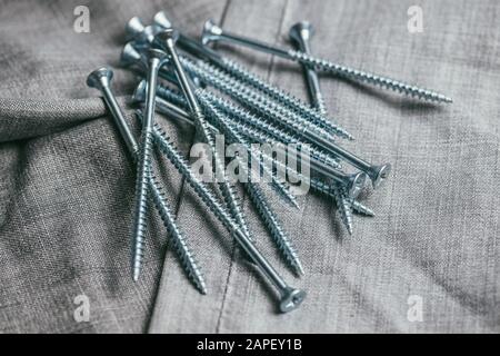 Eine Handvoll metallischer Selbstschneiderschrauben liegt vor dem Hintergrund eines alten Denimstoffs. Selektives Fokusmakro mit flachem Freiheitsgrad. Stockfoto