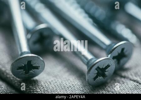 Eine Handvoll metallischer Selbstschneiderschrauben liegt vor dem Hintergrund eines alten Denimstoffs. Selektive Fokusaufnahme mit flachem Freiheitsgrad. Extreme Nahaufnahme. Stockfoto